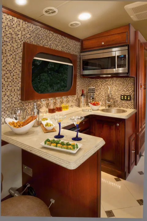 Plush RV rental interior: a fully equipped kitchen & wet bar with cherry wood, mosaic tiles, and elegant serving ware.. Dynamax Corp Grand Sport 2015