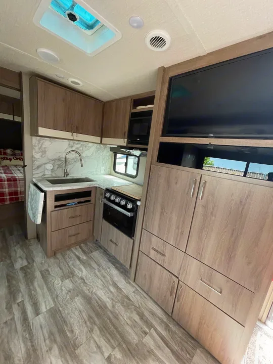 Modern RV rental interior showcasing a well-equipped kitchen with sink, stove, and microwave, plus cozy bedroom area.. Grand Design Imagine 2022