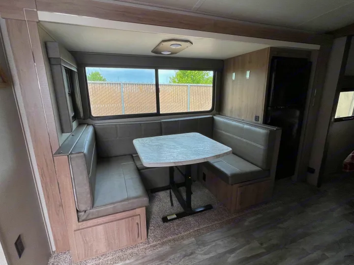 RV rental dinette with U-shaped seating, table, and refrigerator. Ideal for travel trailer living.. Grand Design Imagine 2022