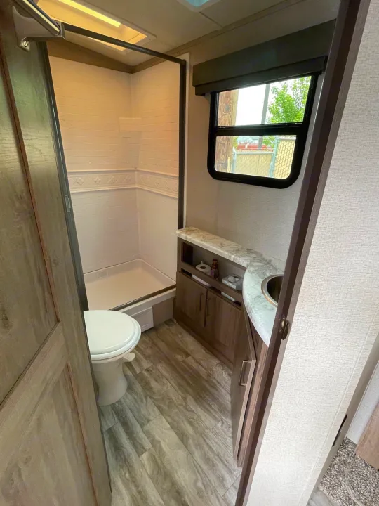 Spacious RV rental bathroom featuring a walk-in shower, toilet, vanity, and window for comfort.. Grand Design Imagine 2022