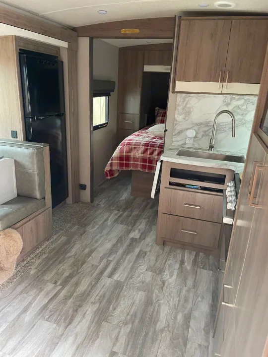 Inside a clean rv rental: well-equipped kitchen with a sink, a cozy dinette, and a comfortable bedroom area.. Grand Design Imagine 2022