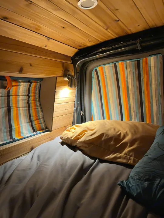 Cozy camper van RV rental interior. Wooden walls, striped curtains, warm light illuminate the bed. Road trip ready!. Gmc Savanna C1500 2014