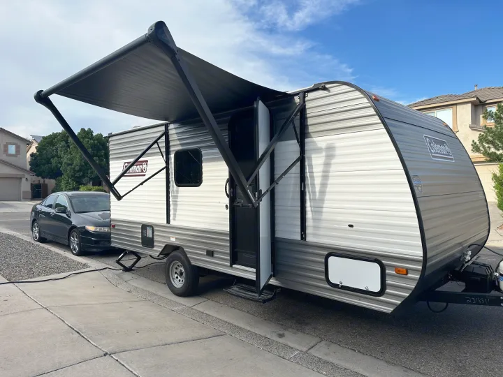 A sleek Coleman travel trailer with an extended awning. Ideal for an rv rental experience, parked on a residential street.. Coleman Lantern 17B 2024