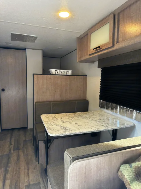 RV rental interior: cozy dining nook with marble-look table, plush booth seating, and light wood cabinetry.. Coleman Lantern 17B 2024