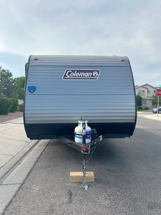 Gray Coleman travel trailer, ready for RV rental, parked roadside with propane tanks & hitch secured.. Coleman Lantern 17B 2024