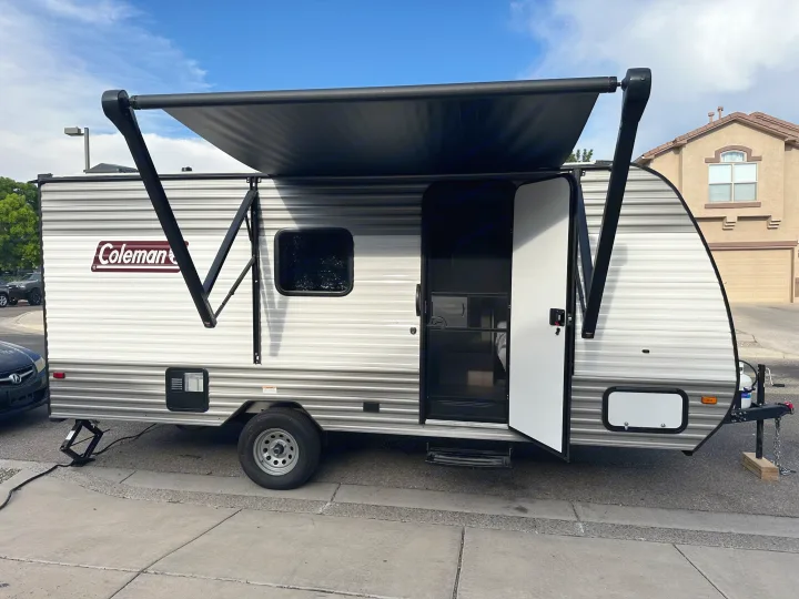 Coleman RV rental: travel trailer with extended awning & open door, parked by a house.. Coleman Lantern 17B 2024
