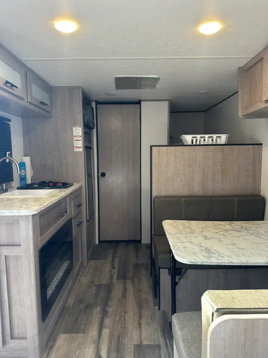 Modern RV rental interior showing a kitchen with marble counters, a comfortable dinette, and light wood cabinetry.. Coleman Lantern 17B 2024