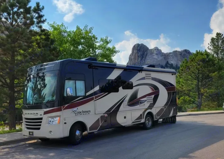 An RV rental is parked, showcasing Mount Rushmore's presidential faces carved into the distant mountain.. Coachman Mirada 2018