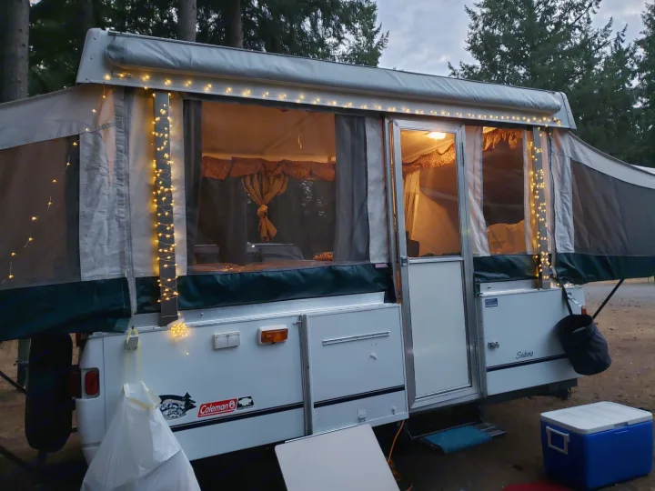 An inviting Coleman Sedona pop-up camper rv rental with warm string lights set up at a dusky campsite.. Coleman Sedona 1999