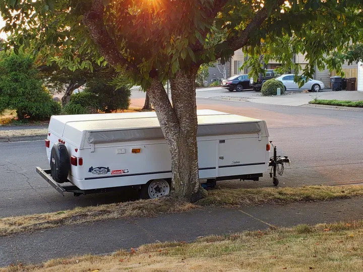 A white Coleman Sedona pop-up RV rental, parked under a sunny tree for your next outdoor adventure.. Coleman Sedona 1999