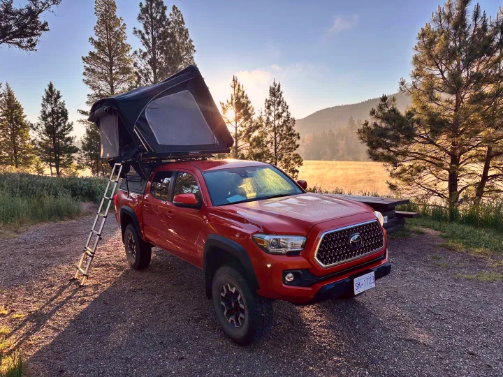 Red Toyota Tacoma with a rooftop tent deployed at a misty lake campsite, perfect for your RV rental adventure.. Toyota Tacoma TRD OFF ROAD 2018