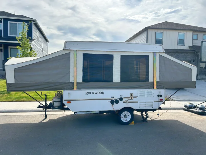 A Rockwood pop-up RV rental, fully set up with canvas sides, is parked on a street. Perfect for camping adventures.. Forest River Rockwood Freedom 2012