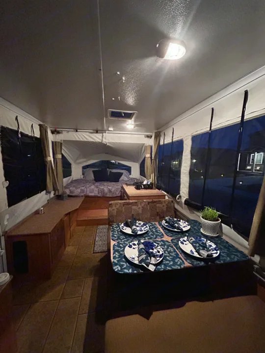 Step inside this cozy RV rental camper, featuring a neatly set dining area, comfortable bed, and warm lighting for a perfect getaway.. Forest River Rockwood Freedom 2012