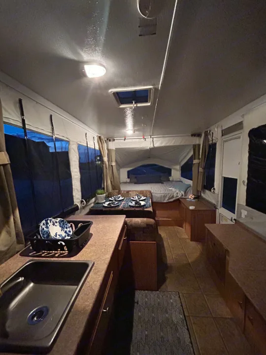 Cozy RV rental interior at dusk. Features include a kitchen sink, dining area, and comfortable bed.. Forest River Rockwood Freedom 2012
