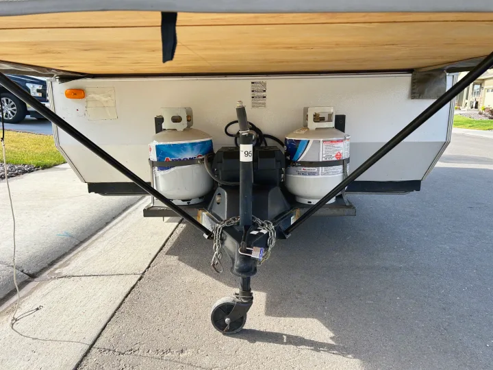 Front view of an RV rental showing its hitch, dual propane tanks, and jack stand, ready for towing.. Forest River Rockwood Freedom 2012