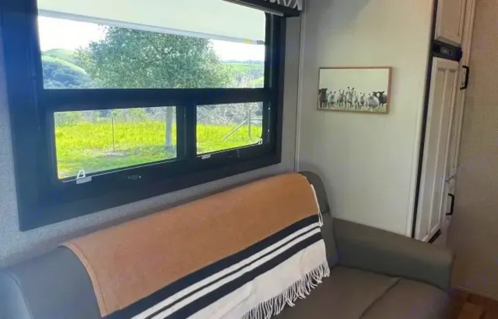 Cozy RV rental interior with a window view of rolling green hills, a comfy sofa, and a fun sheep art piece.. Jayco Greyhawk 2021