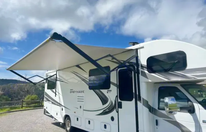 This white Jayco Greyhawk RV rental with an extended awning is parked outdoors under a blue sky, ready for a travel adventure.. Jayco Greyhawk 2021