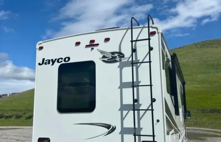 White Jayco RV's rear, featuring a ladder & window under a blue sky, great for rv rental.. Jayco Greyhawk 2021