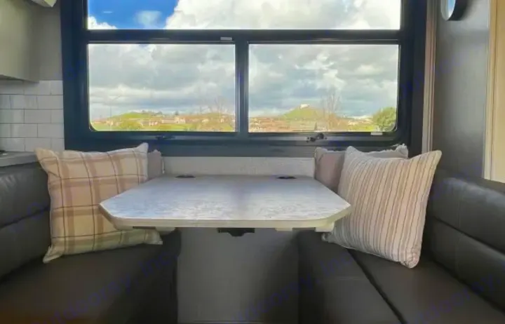 Cozy RV rental dinette with striped and plaid pillows on benches, a table, and large windows offering a hillside view.. Jayco Greyhawk 2021