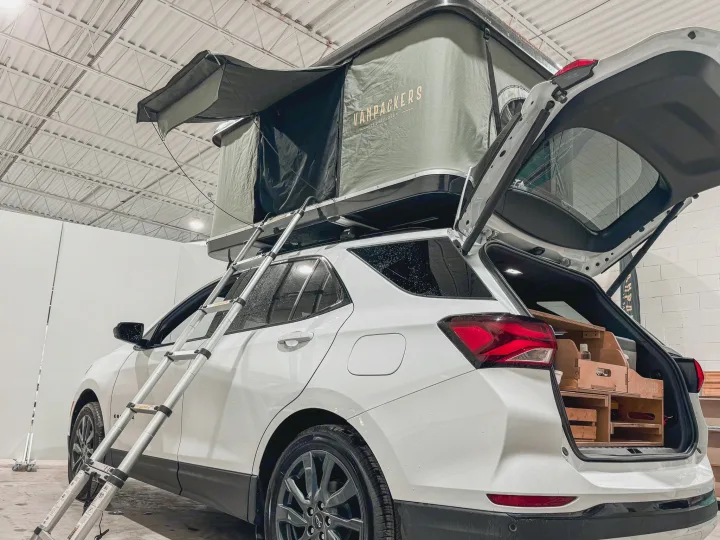 White SUV with a rooftop tent setup & ladder, showcasing interior wooden storage. Ideal for RV rental adventures.. Ford Escape 2025