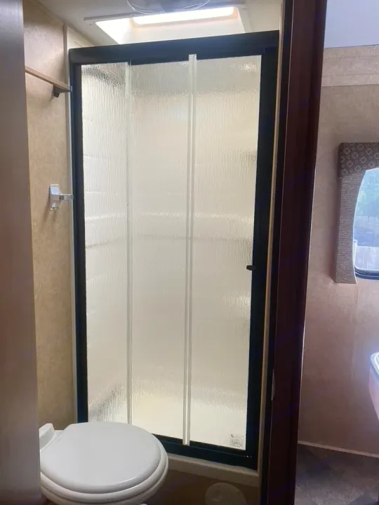 Inside an RV rental: a compact bathroom with a white toilet, enclosed frosted glass shower, and ceiling skylight.. Forest River Sunseeker 2014