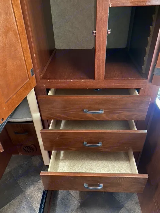 Interior view of an RV rental, showing a brown wooden cabinet with open shelves and three open drawers for storage.. Forest River Sunseeker 2014