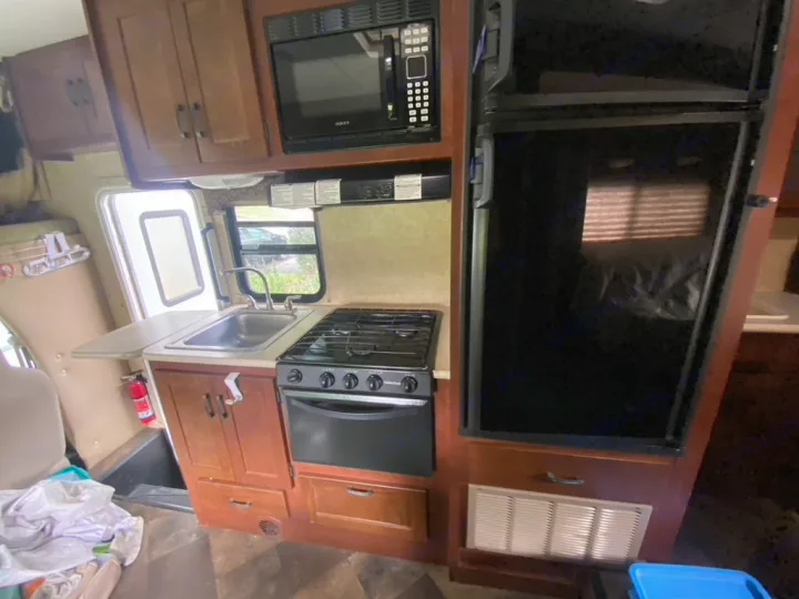 This rv rental kitchen features a sink, stovetop, microwave, fridge, and wooden cabinets. Ideal for travel adventures.. Forest River Sunseeker 2014