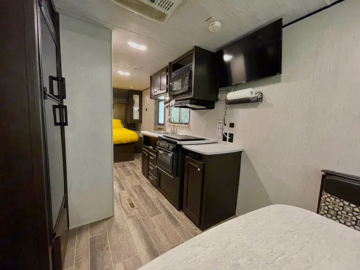 Modern rv rental interior: full kitchen, bedroom (yellow bedding), fridge, and TV. Ideal for road trips and camping adventures.. Heartland RVs Trail Runner SLE 2019