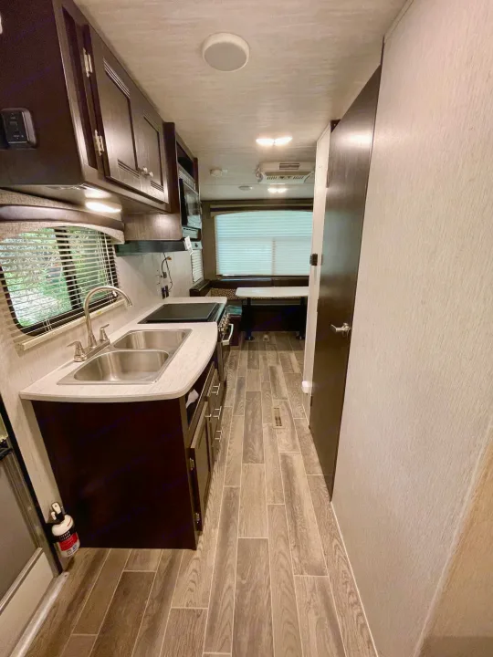 Clean RV rental interior featuring a modern kitchen with double sink, stovetop, and dining area. Wood-look flooring.. Heartland RVs Trail Runner SLE 2019