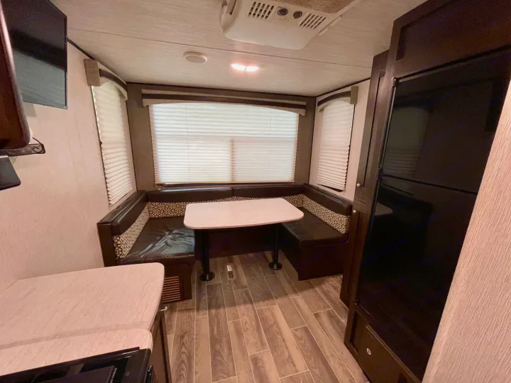 RV rental dinette with U-shaped booth, table, and large windows. Features include a TV, AC, and wood-look flooring.. Heartland RVs Trail Runner SLE 2019