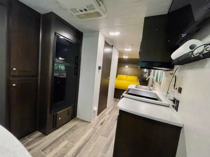 Step inside this cozy RV rental, featuring a compact kitchen with a sink & stove, leading to a comfortable bedroom. Perfect camper living!. Heartland RVs Trail Runner SLE 2019
