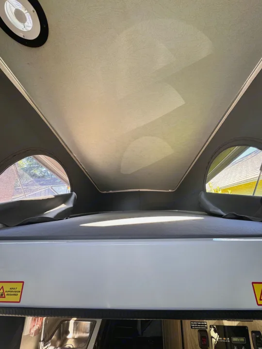 RV rental pop-top bed: View from inside shows sleeping area, side windows, ceiling vent, and lower system controls.. Winnebago Solis 2023