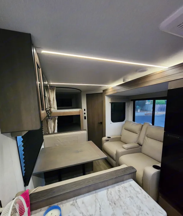 Modern rv rental interior with bright LED lighting, a dining booth, bunk beds, and comfortable recliners.. Grand Design Transcend Xplor 2024