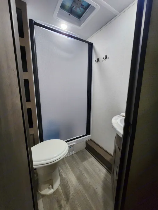 Compact RV rental bathroom featuring a toilet, frosted shower door, and sink. Ideal for travel convenience.. Grand Design Transcend Xplor 2024