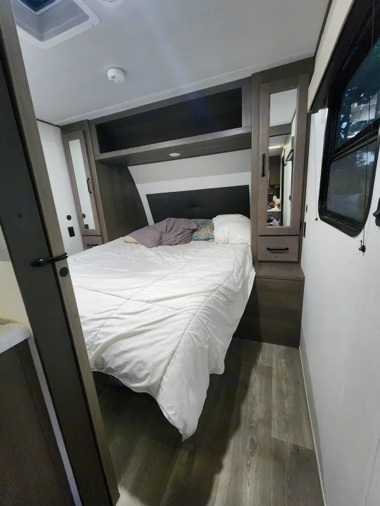 Cozy RV rental bedroom with comfortable bed, built-in storage, and wood-look floor. Ideal for your mobile adventures.. Grand Design Transcend Xplor 2024