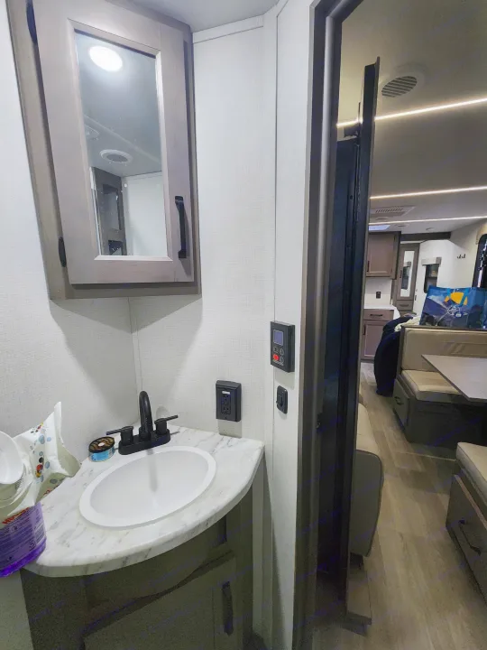 Compact RV rental bathroom with sink, mirror, and controls, opening to a cozy dinette. Ideal for travel.. Grand Design Transcend Xplor 2024