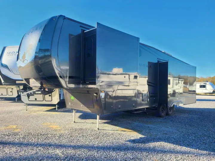 Large black Cougar fifth-wheel RV rental with extended slide-outs, parked on gravel.. Keystone RV Cougar 2024