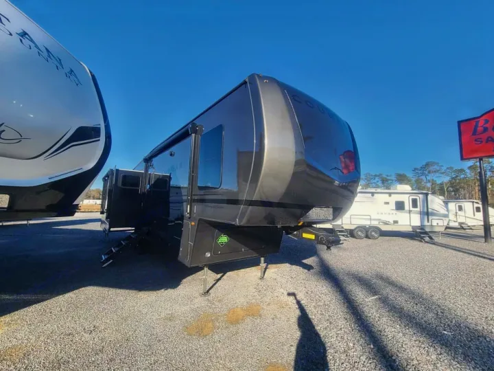 A dark grey Cougar fifth-wheel RV with steps extended on a gravel lot, next to other RVs. Perfect for an rv rental.. Keystone RV Cougar 2024