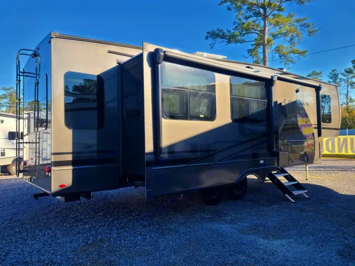 Modern gray Cougar fifth-wheel RV rental on gravel, with slide-outs extended for spacious living and an awning deployed.. Keystone RV Cougar 2024