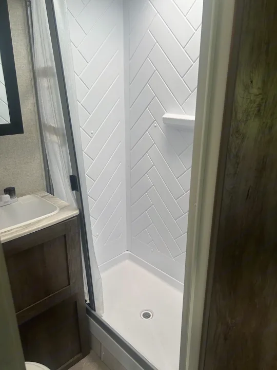 Clean RV rental bathroom featuring a modern white shower with herringbone walls and a vanity sink.. Forest River Salem Cruise Lite 2021