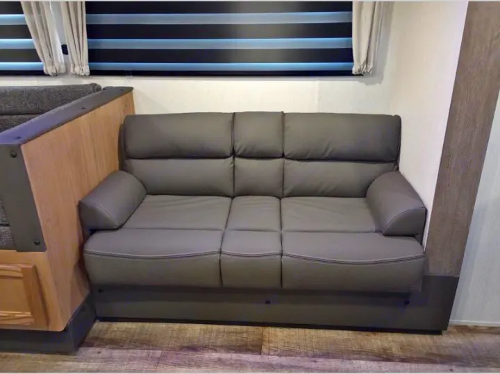 Comfortable gray sofa inside an RV rental, offering cozy seating with modern design and striped window blinds.. Forest River Cherokee Grey Wolf 2024