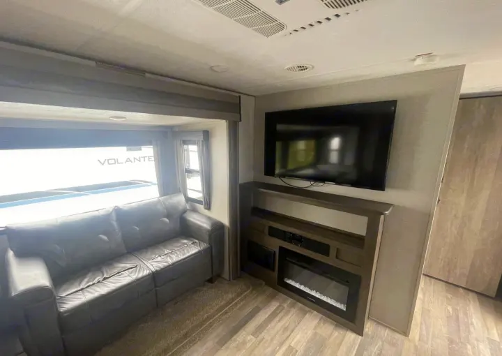 Cozy RV rental living area. Features a dark sofa, window, and entertainment unit with TV & electric fireplace.. Forest River Vibe 2020