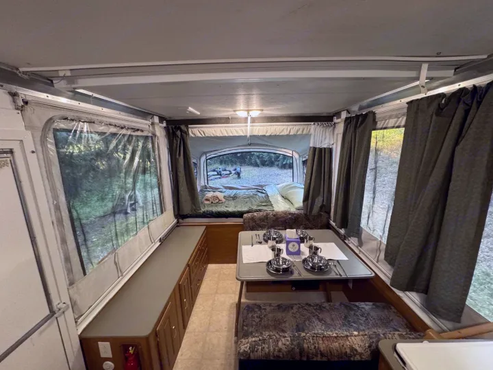 Spacious pop-up RV rental interior: cozy dinette, comfortable beds, and forest views at the campsite.. Fleetwood Santa Fe 2004
