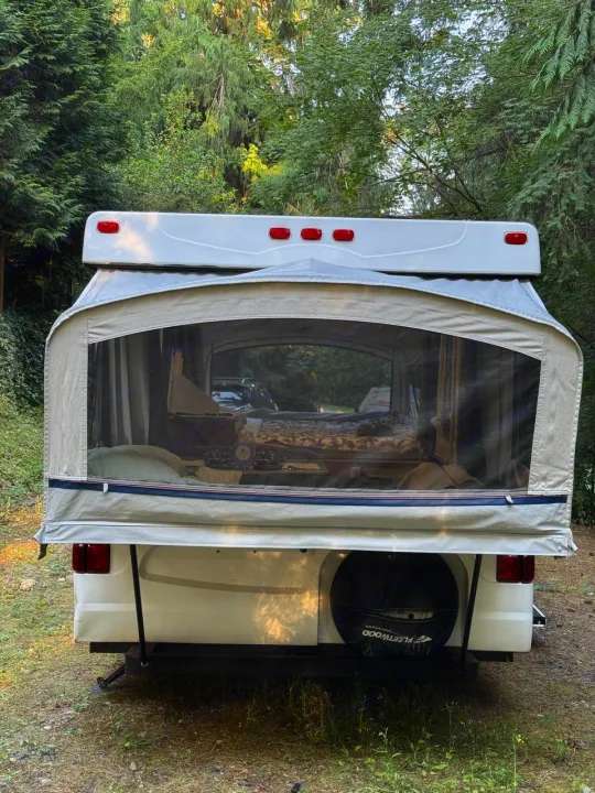 Back view of an RV rental: a pop-up camper in a wooded campsite, showing interior bed. Great for camping trips.. Fleetwood Santa Fe 2004