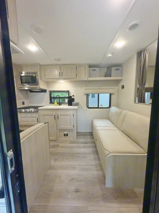 Clean RV rental interior: kitchen with stove/microwave, comfy sofa, and wood-look floors.. Coachmen 261BH 2024