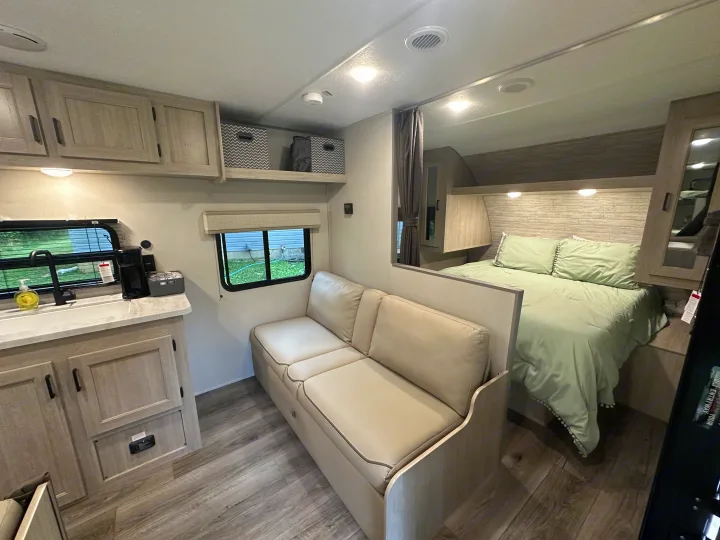 Spacious RV rental interior with kitchen, sofa, and bedroom area, featuring light wood tones.. Coachmen 261BH 2024