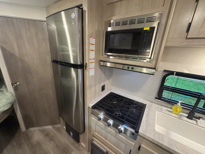 Modern RV rental kitchen featuring stainless steel GE refrigerator, microwave, and a 3-burner stovetop with a sink.. Coachmen 261BH 2024