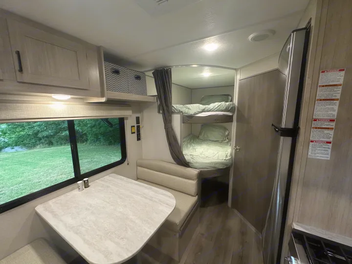 A practical RV rental interior featuring a dinette with window view, cozy bunk beds, and essential kitchen amenities.. Coachmen 261BH 2024