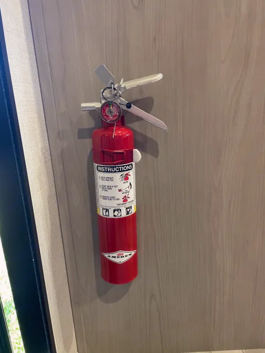 Red fire extinguisher mounted on a light wood wall inside an RV rental, essential for fire safety.. Keystone Springdale 1800BH 2024