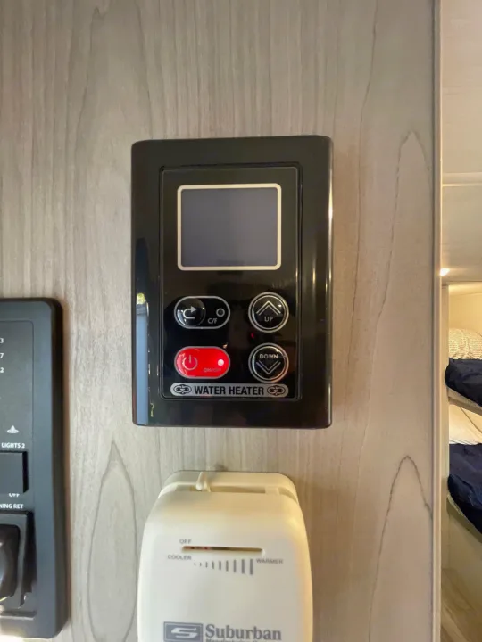 This RV rental image shows black digital water heater controls (screen, up/down, on/off buttons) above a white Suburban thermostat.. Keystone Springdale 1800BH 2024